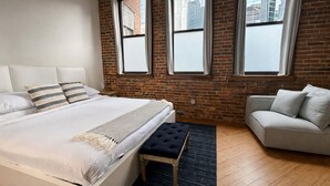 A modern bedroom with a large bed, a bench, and a grey sofa. - Downtown Music City Loft living! ~Steps to the Ryman and Broadway. (Nashville)