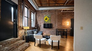 A spacious living area with a brick wall, a sofa, a coffee table, and two chairs. - Downtown Music City Loft living! ~Steps to the Ryman and Broadway. (Nashville)