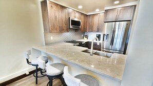A modern kitchen with a marble countertop, stainless steel appliances, and wooden cabinets. - On Lake! Updated Penthouse! Pool, Hot Tub, Elevator. Walk to Concerts, Dining (Dillon)