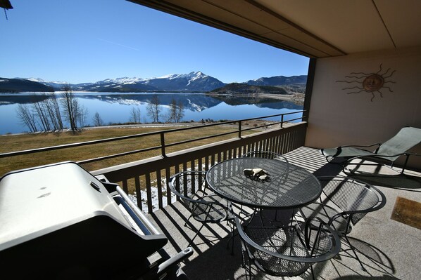A balcony with a view of a lake and mountains, furnished with metal chairs and a table.