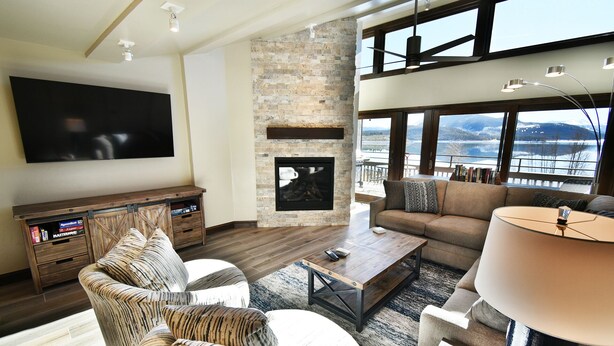 A modern living room with a fireplace, a large TV, and a view of a lake. - On Lake! Updated Penthouse! Pool, Hot Tub, Elevator. Walk to Concerts, Dining (Dillon)