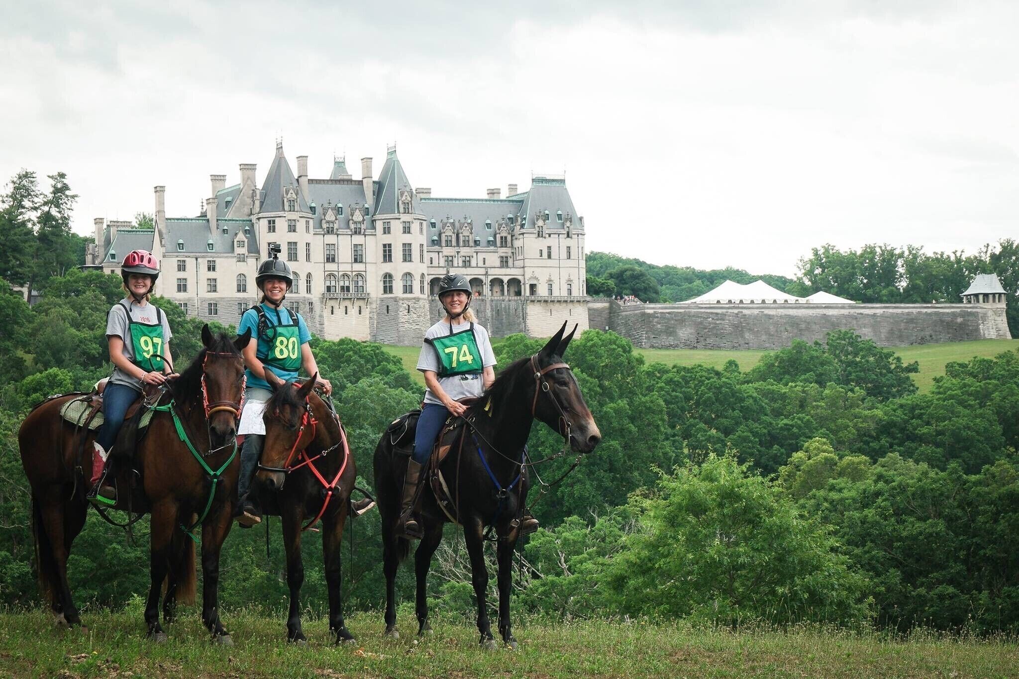 Drie ruiters op paarden voor een groot, historisch gebouw met een kasteelachtige uitstraling.
