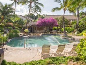 A pool area with lounge chairs, palm trees, and a building in the background.