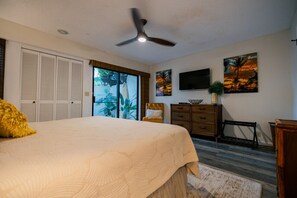 A bedroom with a bed, a ceiling fan, a TV, and artwork on the wall.