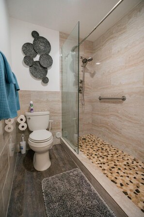 A modern bathroom with a glass shower enclosure, a toilet, and a decorative wall piece.