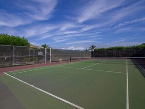An outdoor tennis court with a net, surrounded by a low wall and trees.