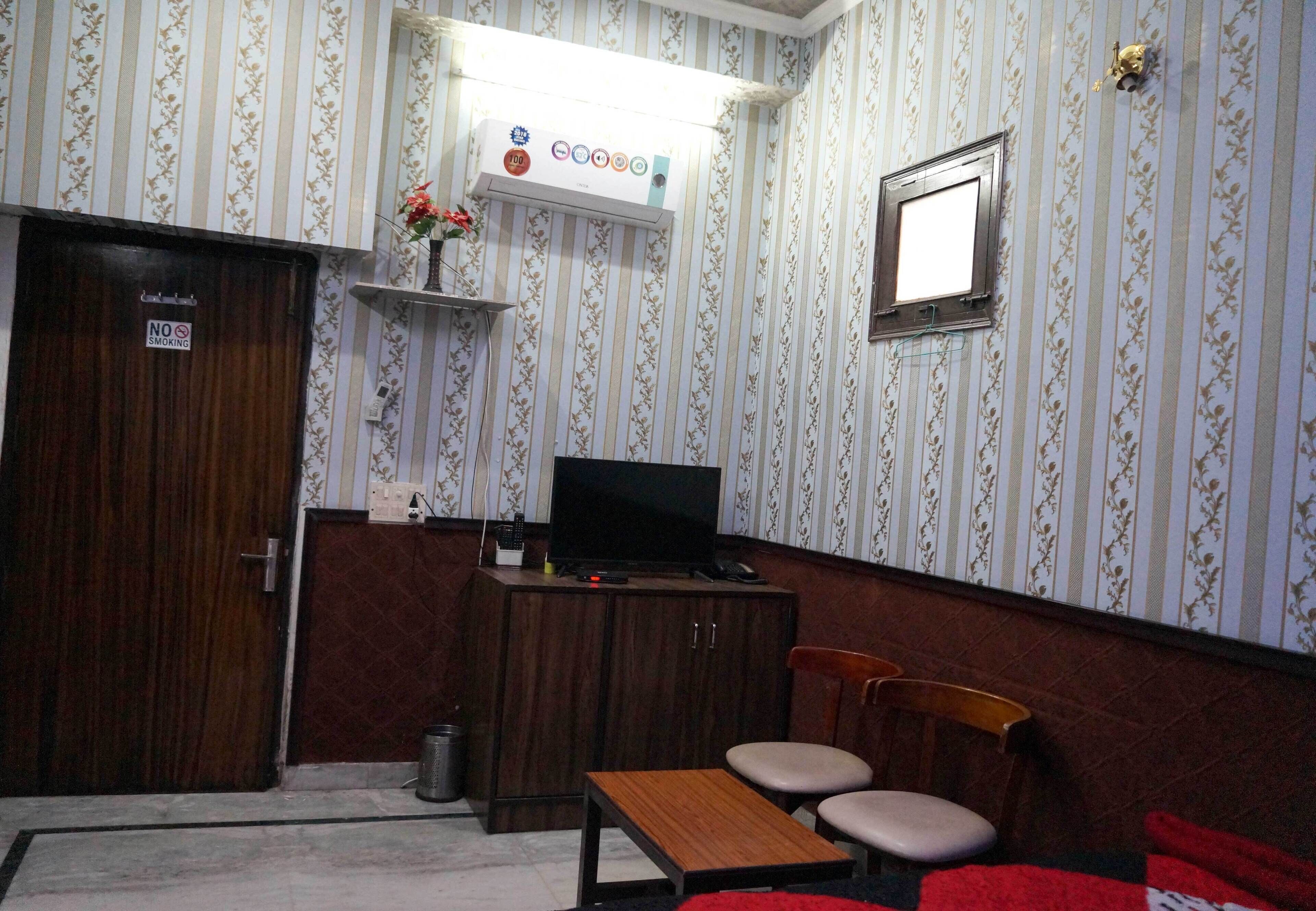 A room with striped wallpaper, a wooden desk with a television, a chair, and a small table.