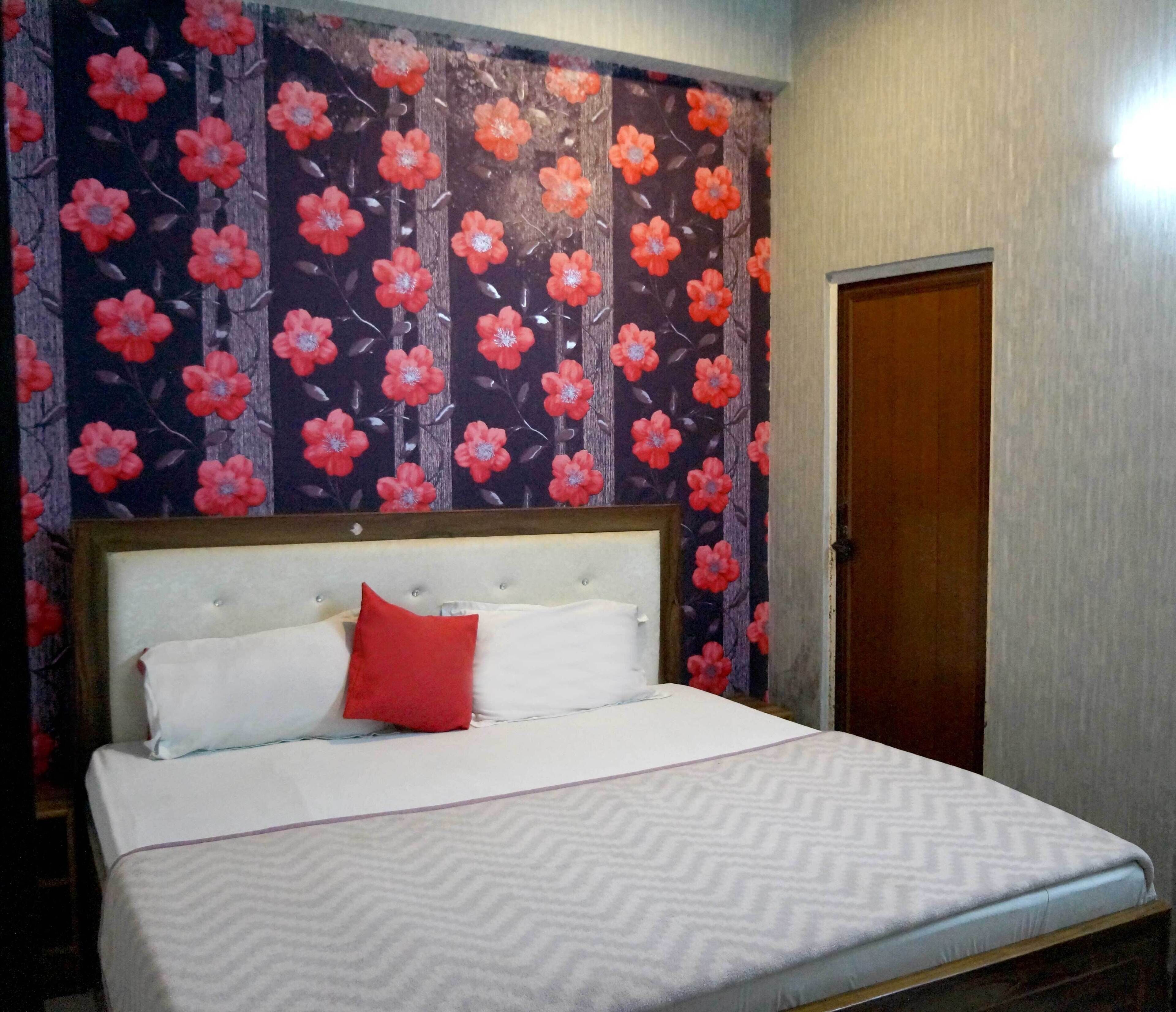 A bed with a white and red patterned bedspread, a red pillow, and a wooden headboard.