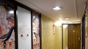 A hotel corridor with framed posters, a red carpet, and a wooden door. - Osaka Taj Hotel (Agra)