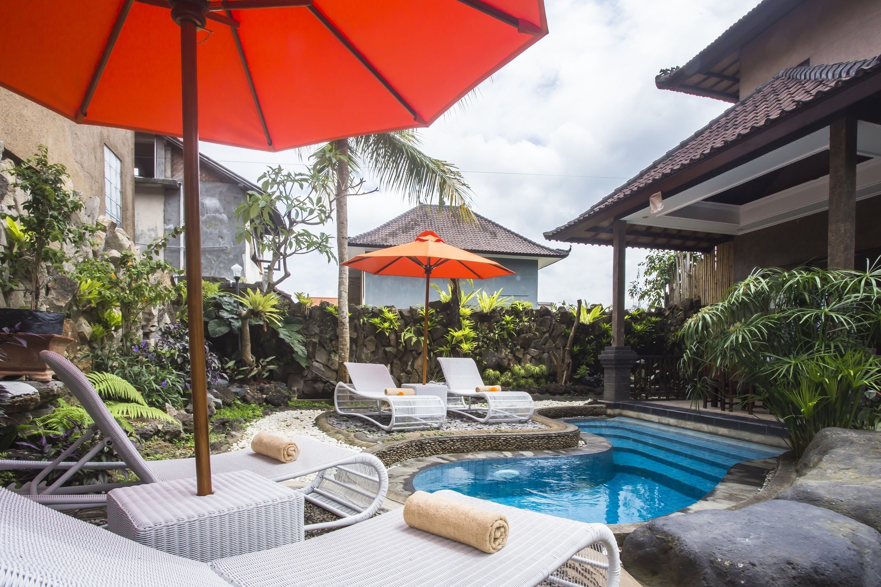 A pool area with lounge chairs, a red umbrella, and a stone wall.