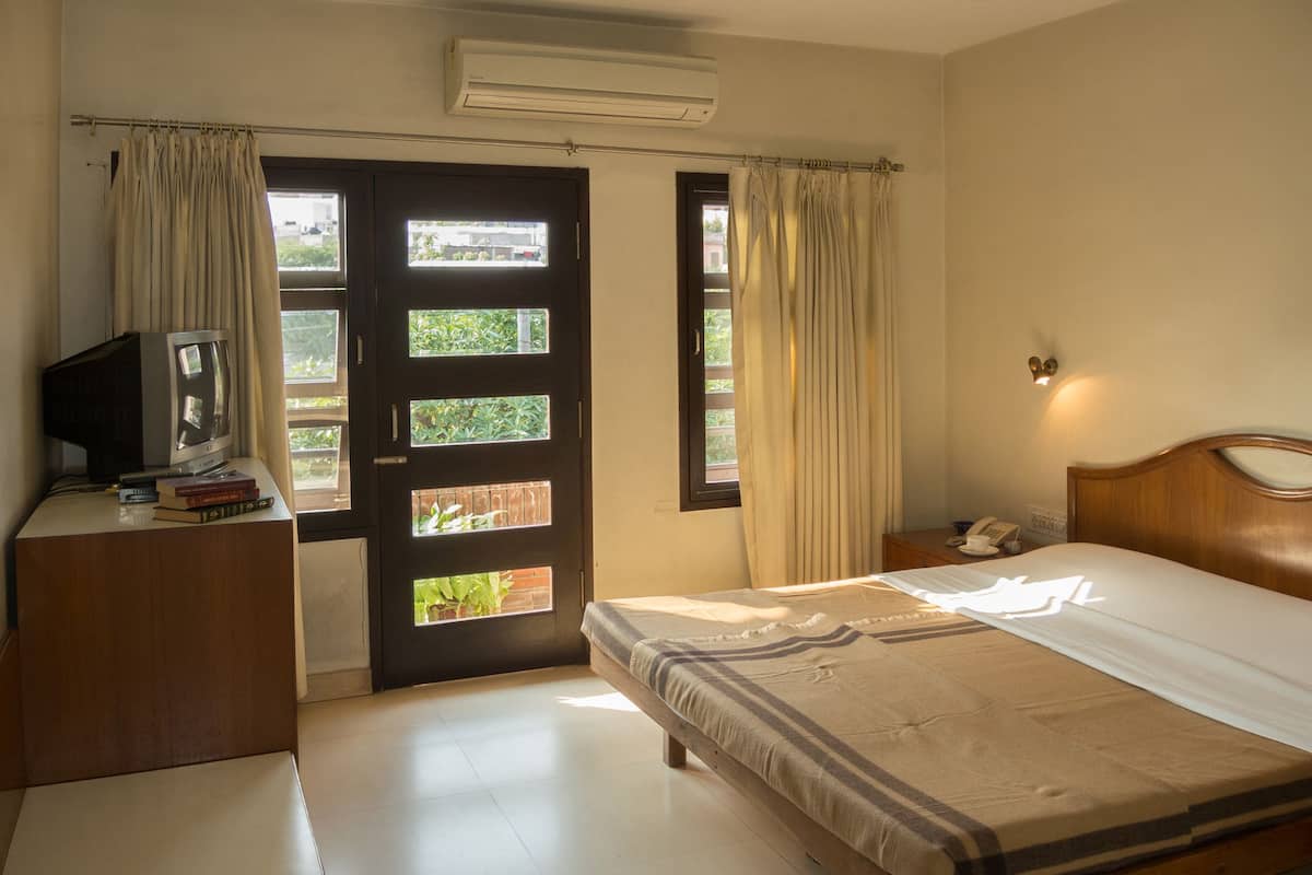 A hotel room with a bed, a desk with a television and books, a telephone, and a window with curtains.