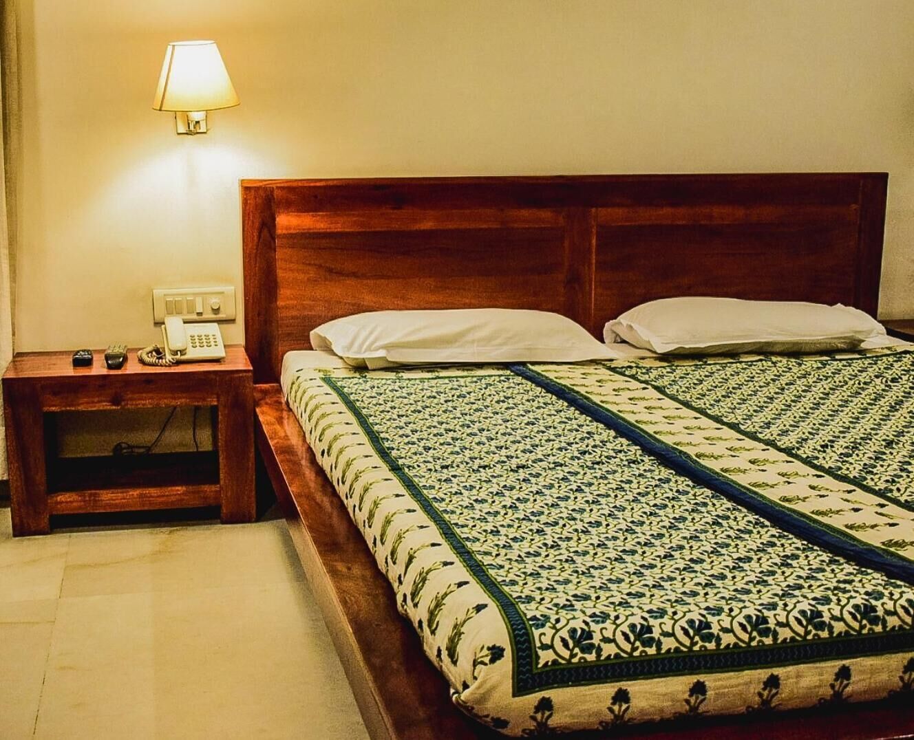 Una cama bien hecha con una colcha estampada, una mesita de noche con lámpara y un teléfono.