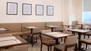 A hotel dining area with tables and chairs, framed artwork on the wall, and a large window. - Capital O 827 Speciale Hotel (Rosario)