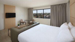 A hotel room with a large bed, a TV mounted on the wall, a small seating area with a table and chairs, and a view of the city through the window. - Capital O 827 Speciale Hotel (Rosario)