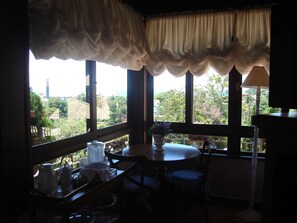 Ein Zimmer mit Esstisch, Stühlen, einem fenster mit Vorhängen und Blick auf Grünflächen und Gebäude.