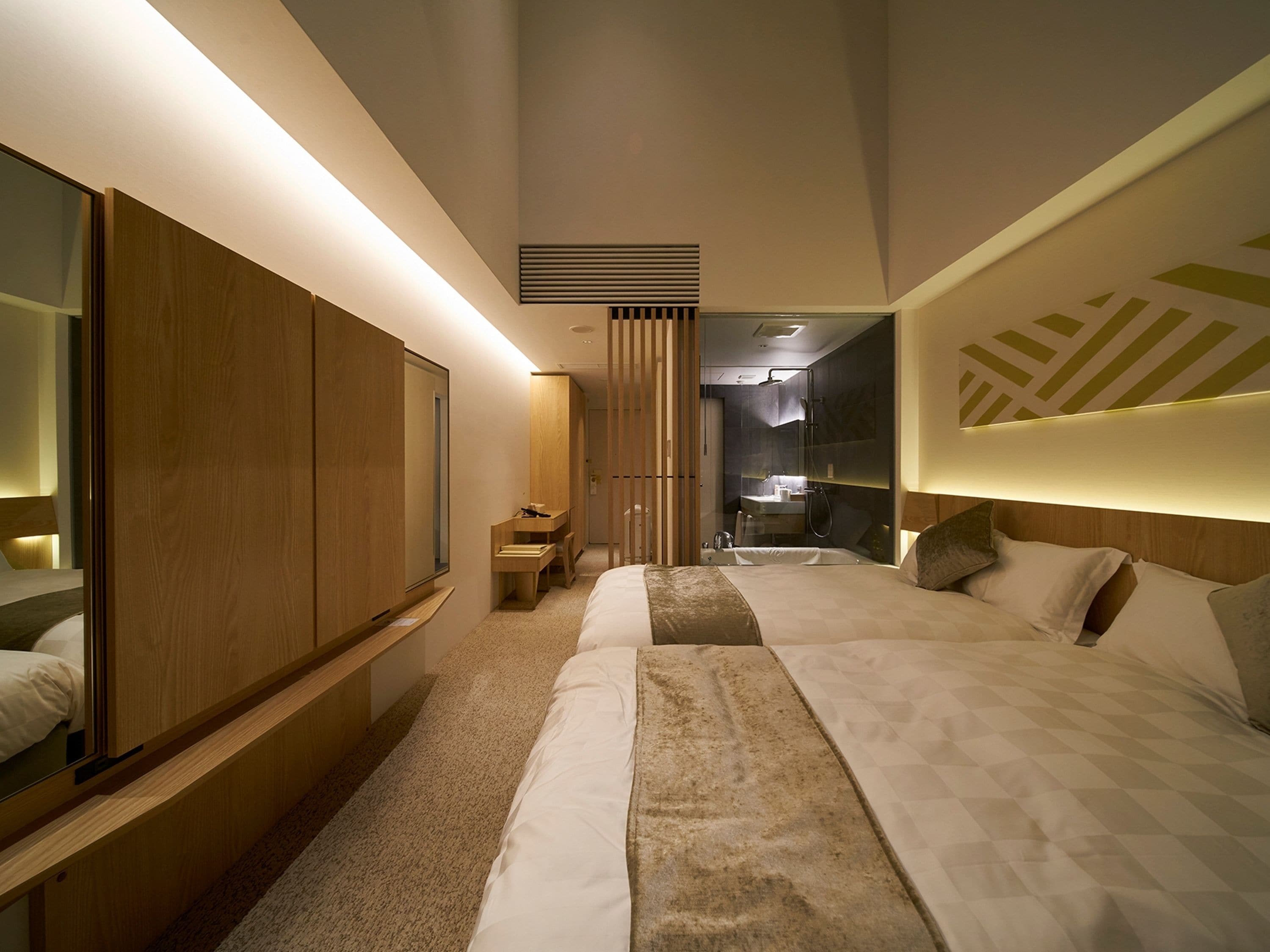 Ein modernes Hotelzimmer mit einem großen Bett, einem Holzschrank, einem kleinen Schreibtisch und einem Badezimmer mit Dusche und Waschbecken.
