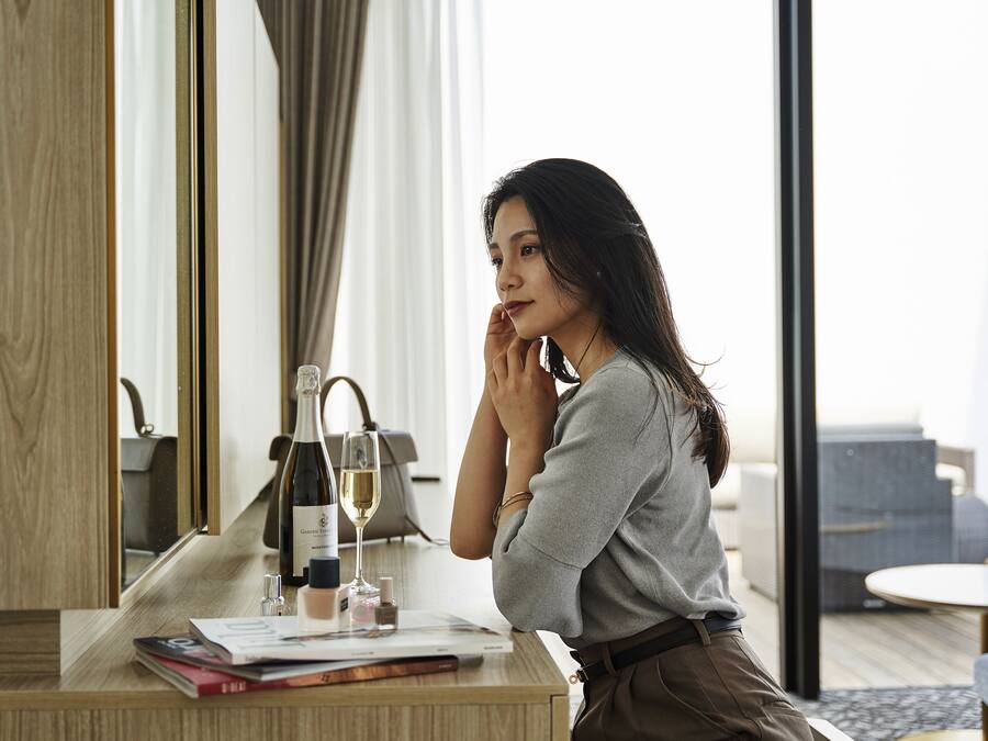 A woman sitting at a wooden desk with a bottle of wine, a glass, and some books.