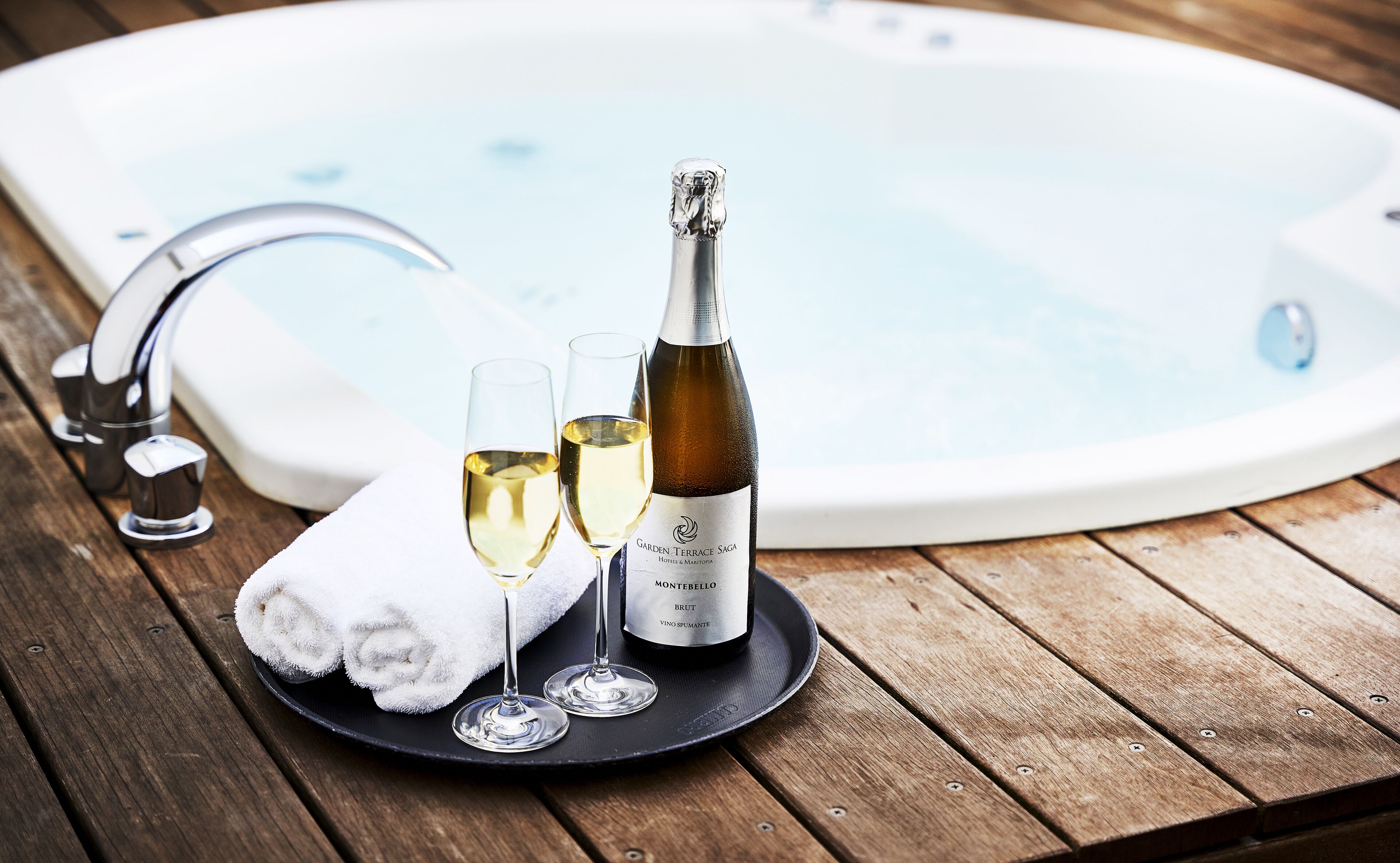 Une table en bois, un jacuzzi, une bouteille de vin et deux verres.