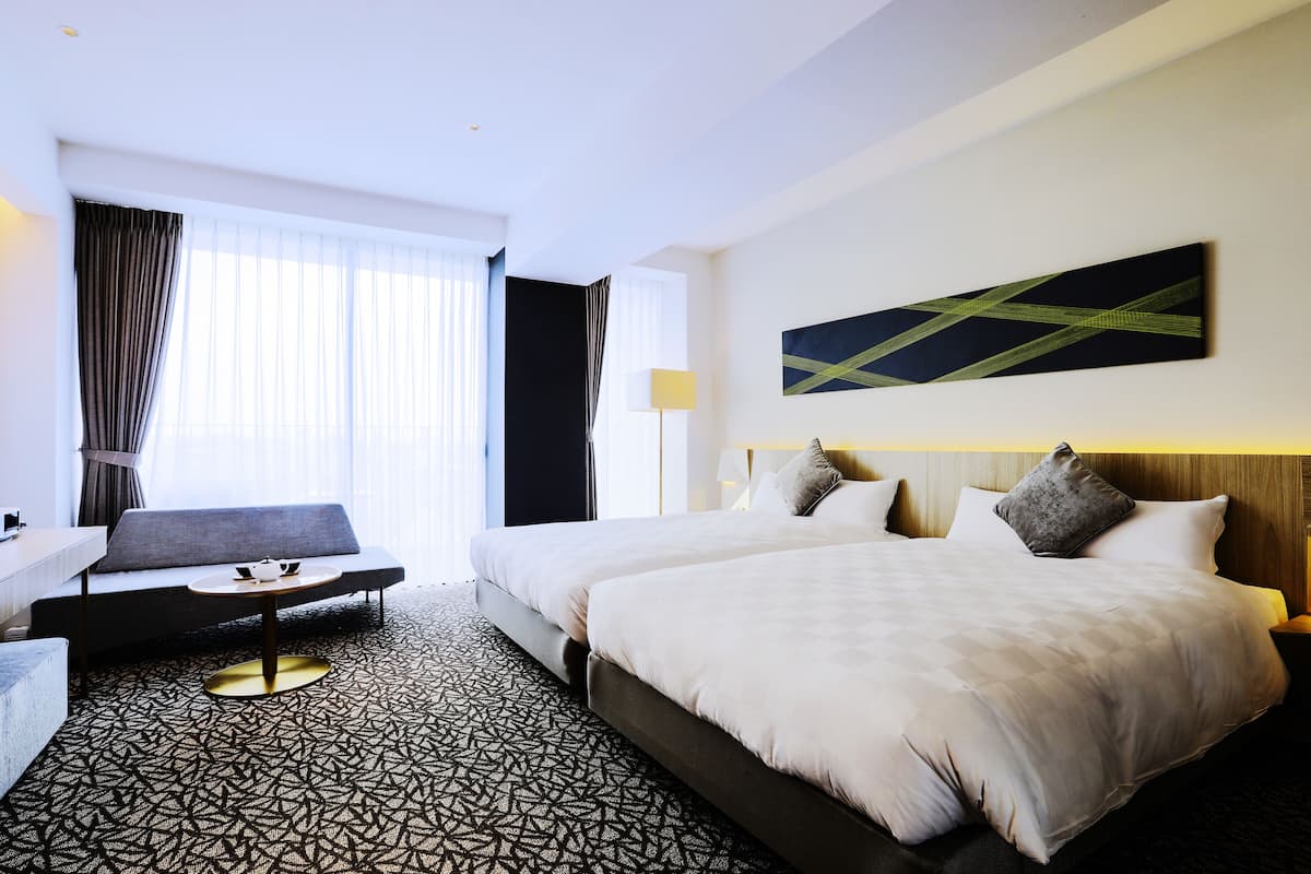 A hotel room with a large bed, a sofa, a small table, and a painting on the wall.