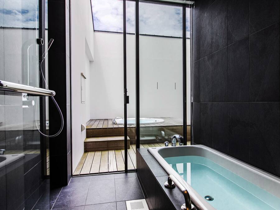 A modern bathroom with a bathtub, a glass shower enclosure, and a view of a wooden deck and outdoor area.