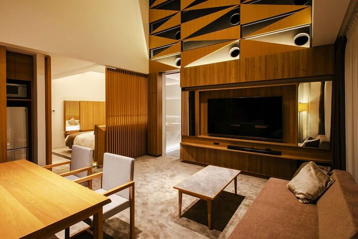 A modern hotel room with a wooden floor, a TV, a sofa, a dining table, and a bed.