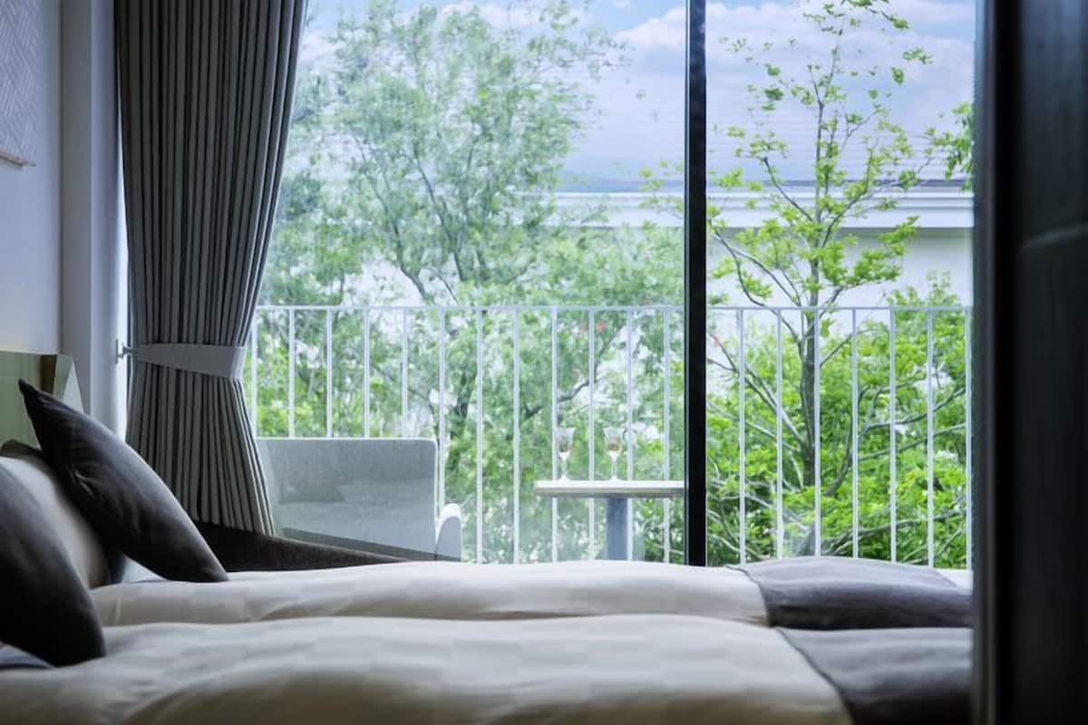 A bedroom with a bed, pillows, a window with curtains, and a balcony with a railing.