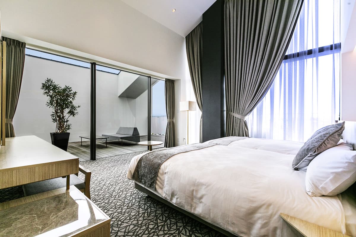 A modern hotel room with a large bed, a dining table, and a potted plant.