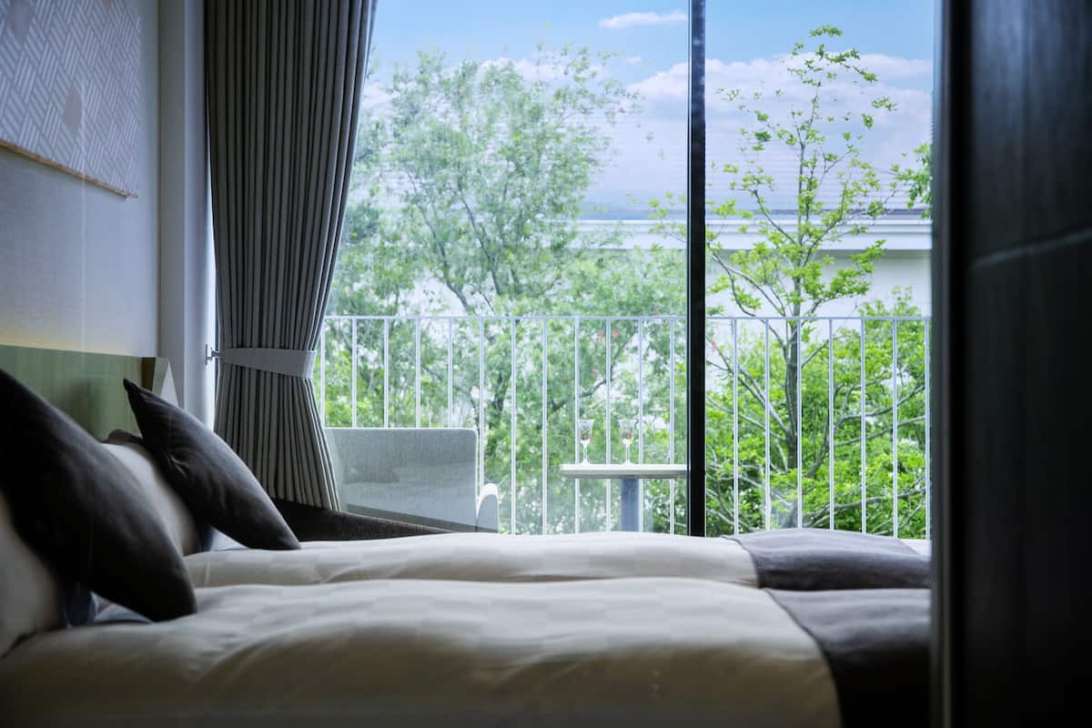 A hotel room with a bed, curtains, and a view of a balcony with trees and a railing.