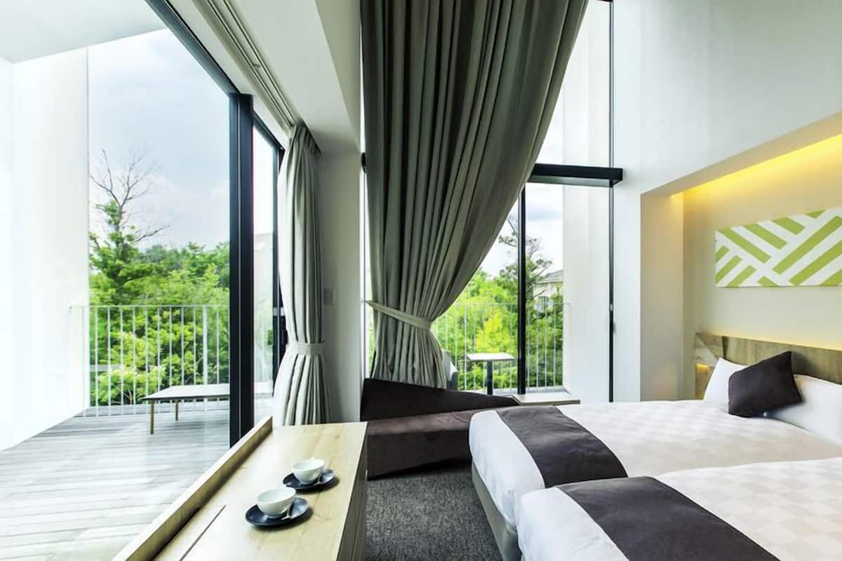 A hotel room with a bed, a table with bowls, a view of greenery outside, and a geometric wall decoration.