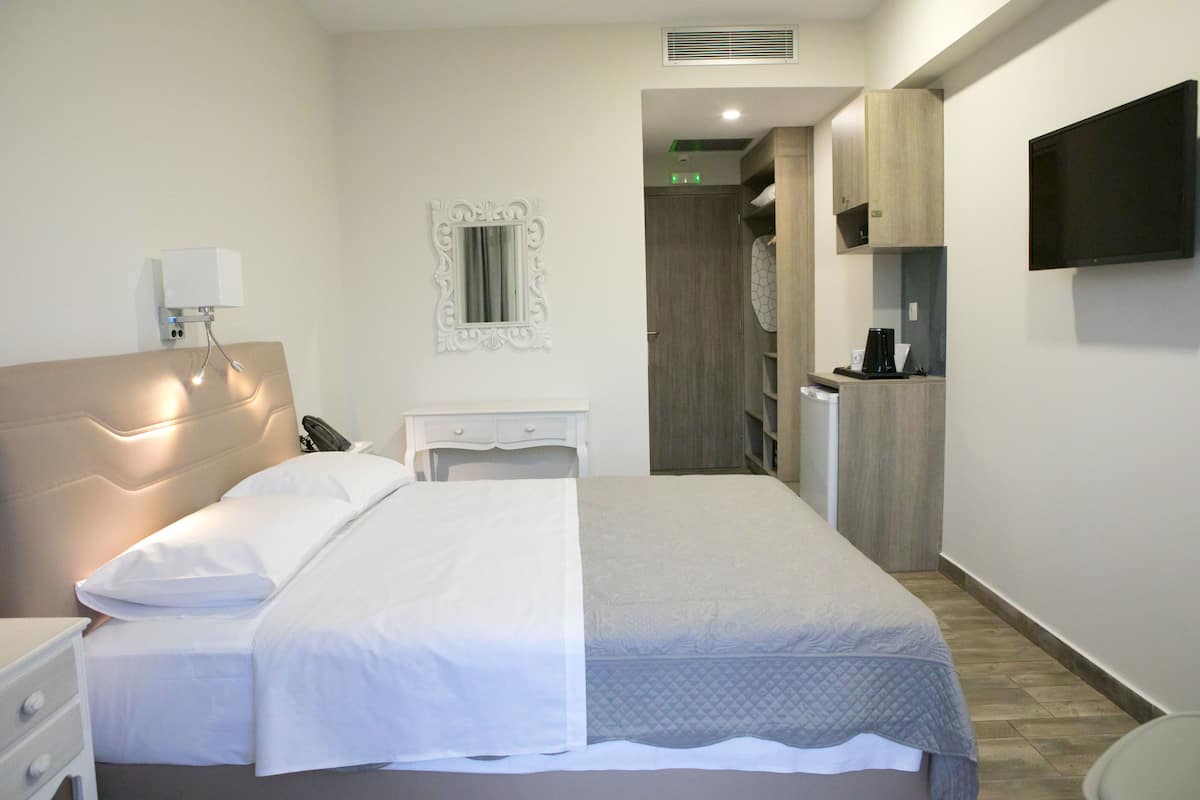Ein modernes Hotelzimmer mit einem großen Bett, Nachttischen, einem Spiegel, einem Flachbildfernseher und einer Küchenzeile.