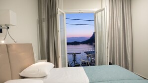 A hotel room with a bed, a nightstand, and a view of a body of water and a distant mountain range through an open door. - Hyperion Hotel Kalymnos (Kalymnos)
