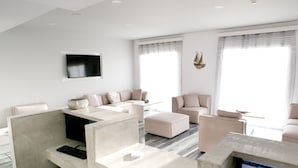 A modern hotel room with a large window, a flat-screen TV, a sofa, a desk with a computer, and a small table. - Hyperion Hotel Kalymnos (Kalymnos)