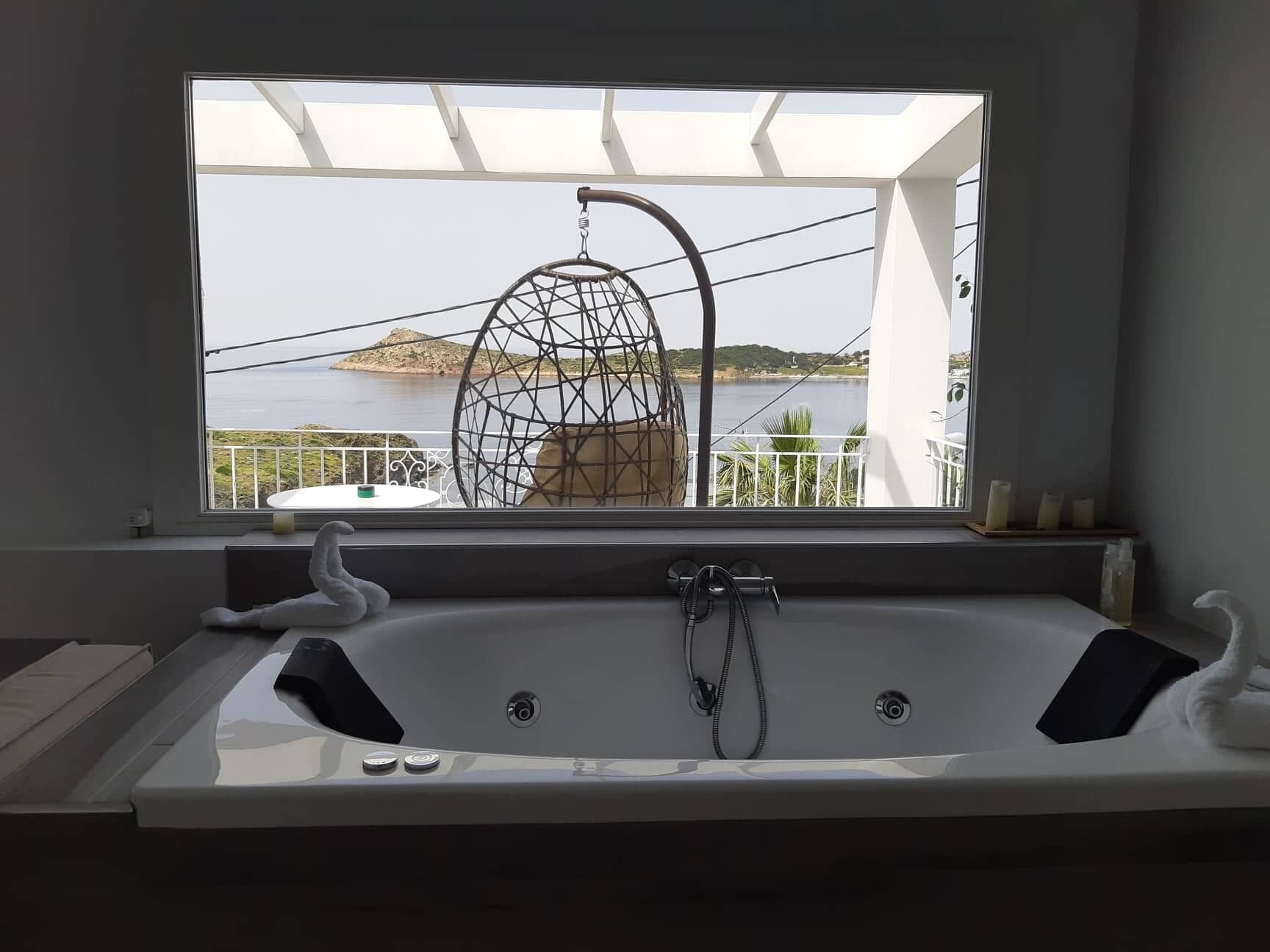 Un baño moderno con una bañera grande, vistas al mar y una silla colgante.