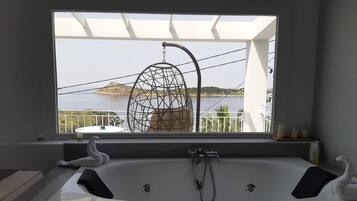 Un baño moderno con una bañera grande, vistas al mar y una silla colgante.