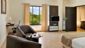A hotel room with a bed, a desk with a lamp, a chair, a TV, and a window with curtains. - The Fern Residency Parbhani (Parbhani)