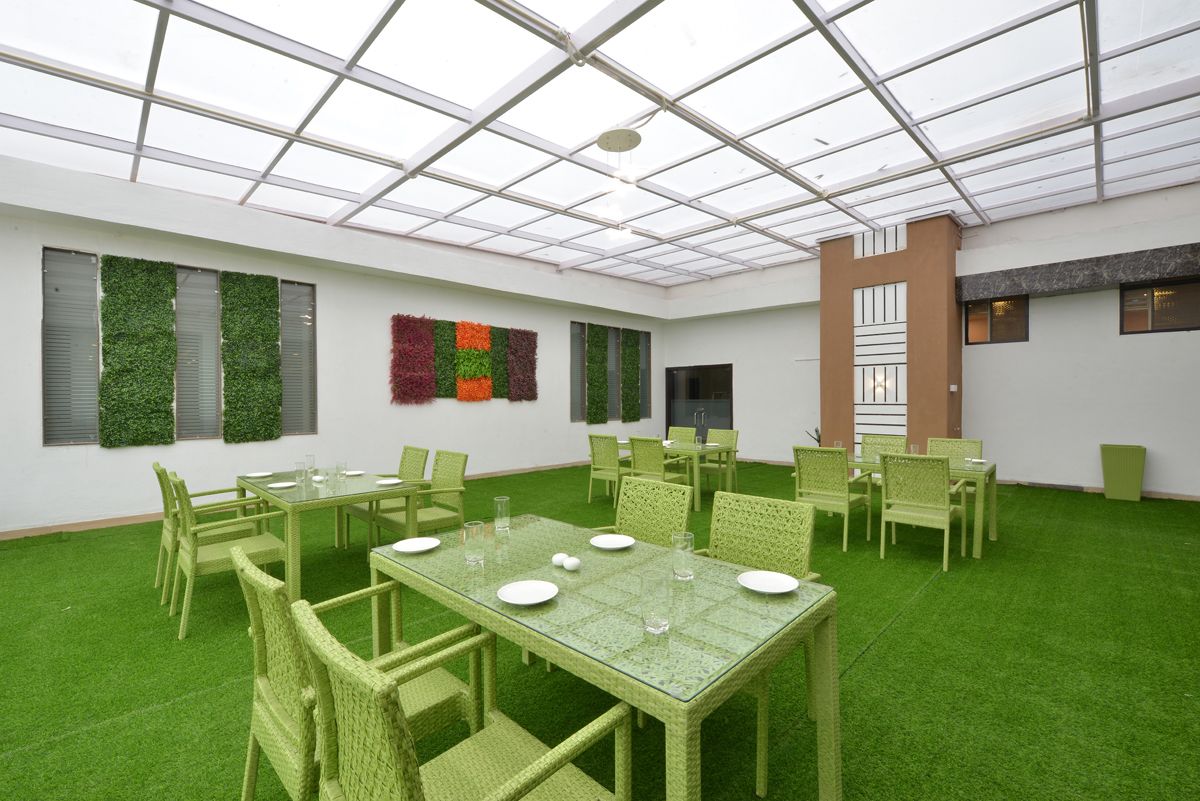 Un'ampia sala da pranzo interna con pavimento in erba sintetica verde, sedie in vimini verde e un tavolo in vetro apparecchiato per un pasto.