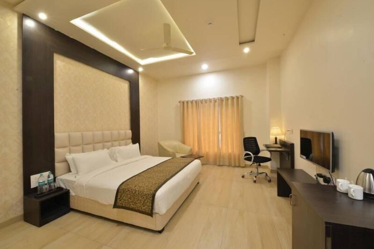 Quarto de hotel com cama, escrivaninha, cadeira, televisão e cortinas.