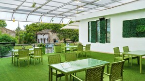 A covered outdoor seating area with green artificial grass, wicker furniture, and a glass table. - The Fern Residency Parbhani (Parbhani)