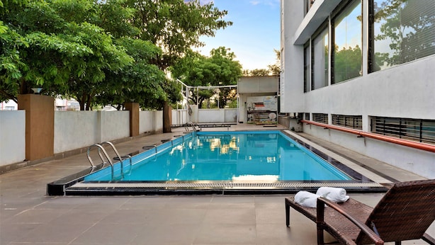 A rectangular swimming pool with a metal ladder, surrounded by a concrete deck. There are two wicker lounge chairs with towels on them. - The Fern Residency Parbhani (Parbhani)