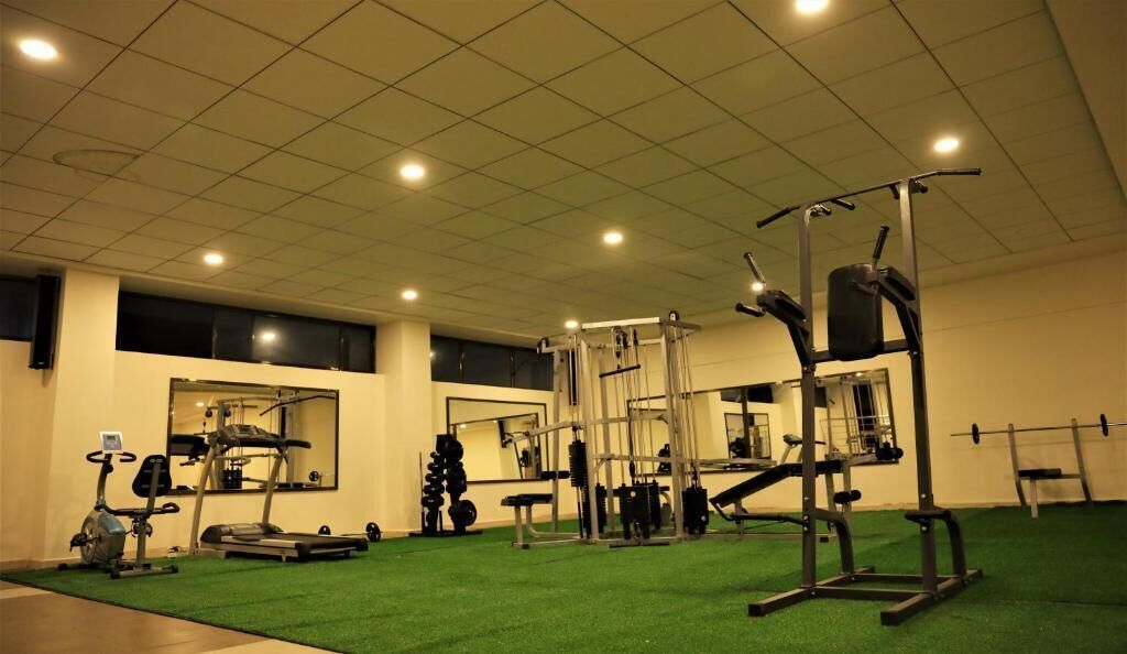 A gym with exercise equipment, green flooring, and a mirrored wall.