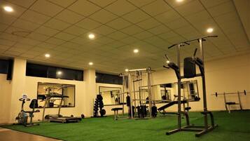 Ein Fitnessstudio mit Trainingsgeräten, grünem Boden und einer Spiegelwand.