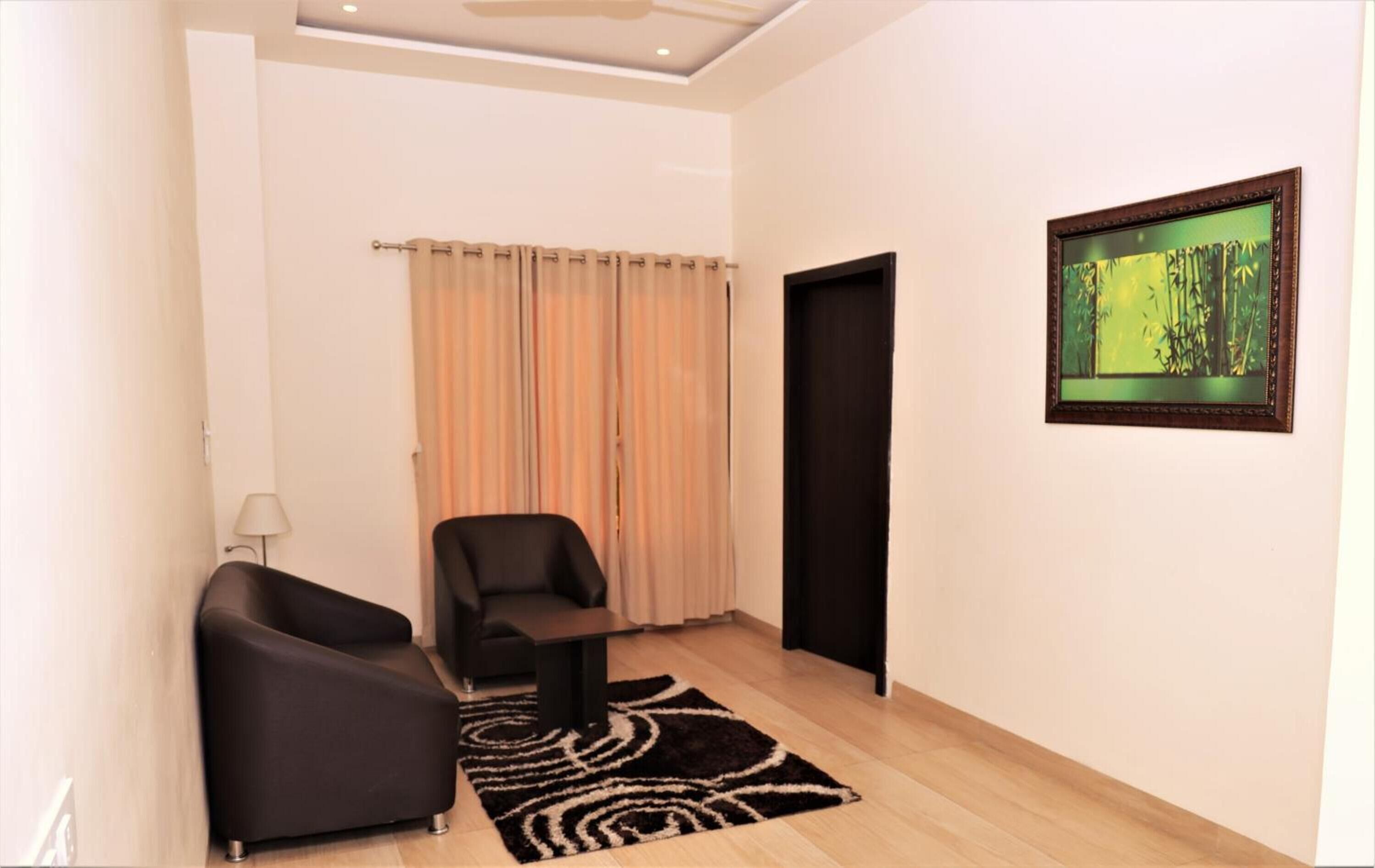 Une pièce moderne avec un canapé noir, une petite table, un tapis à motifs et un tableau encadré au mur.