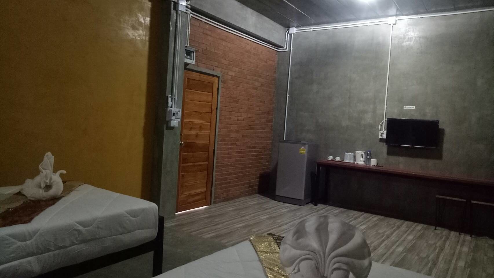 A hotel room with a bed, a small desk, a television, and a refrigerator.