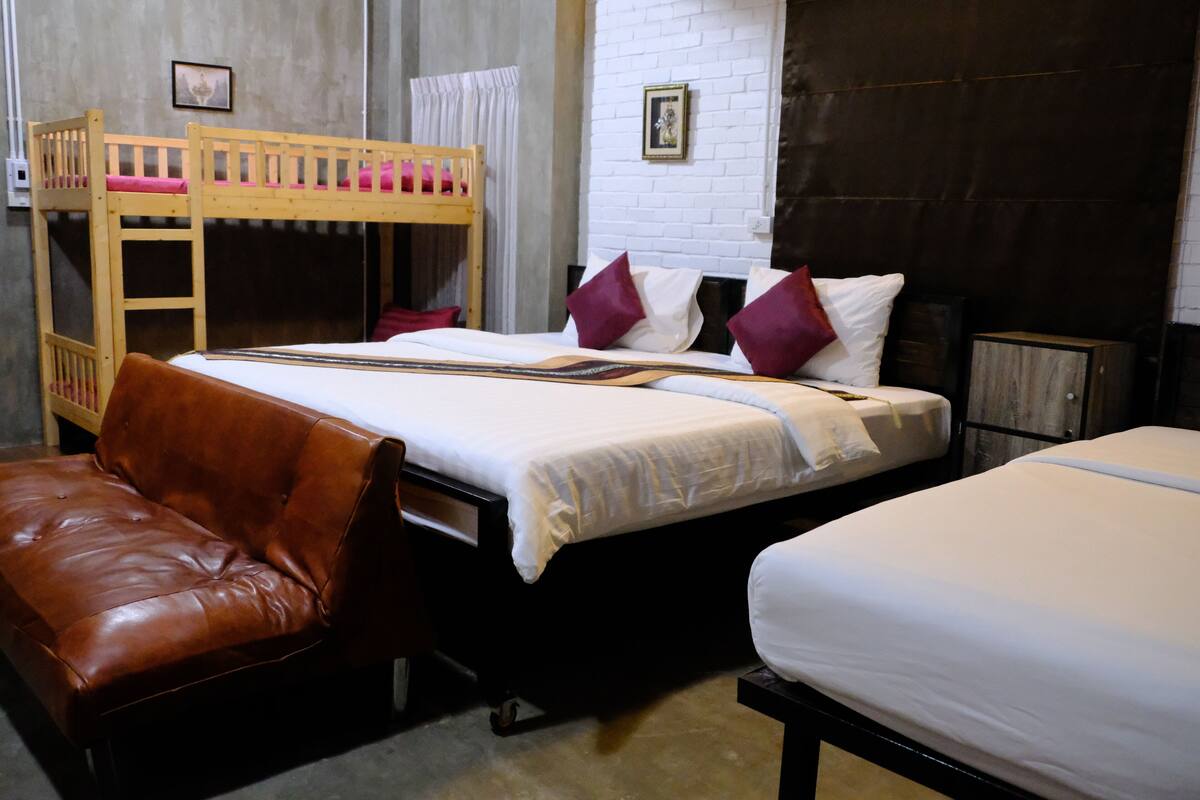 A room with a bunk bed, a single bed, a brown leather chair, and a white wall with a picture.