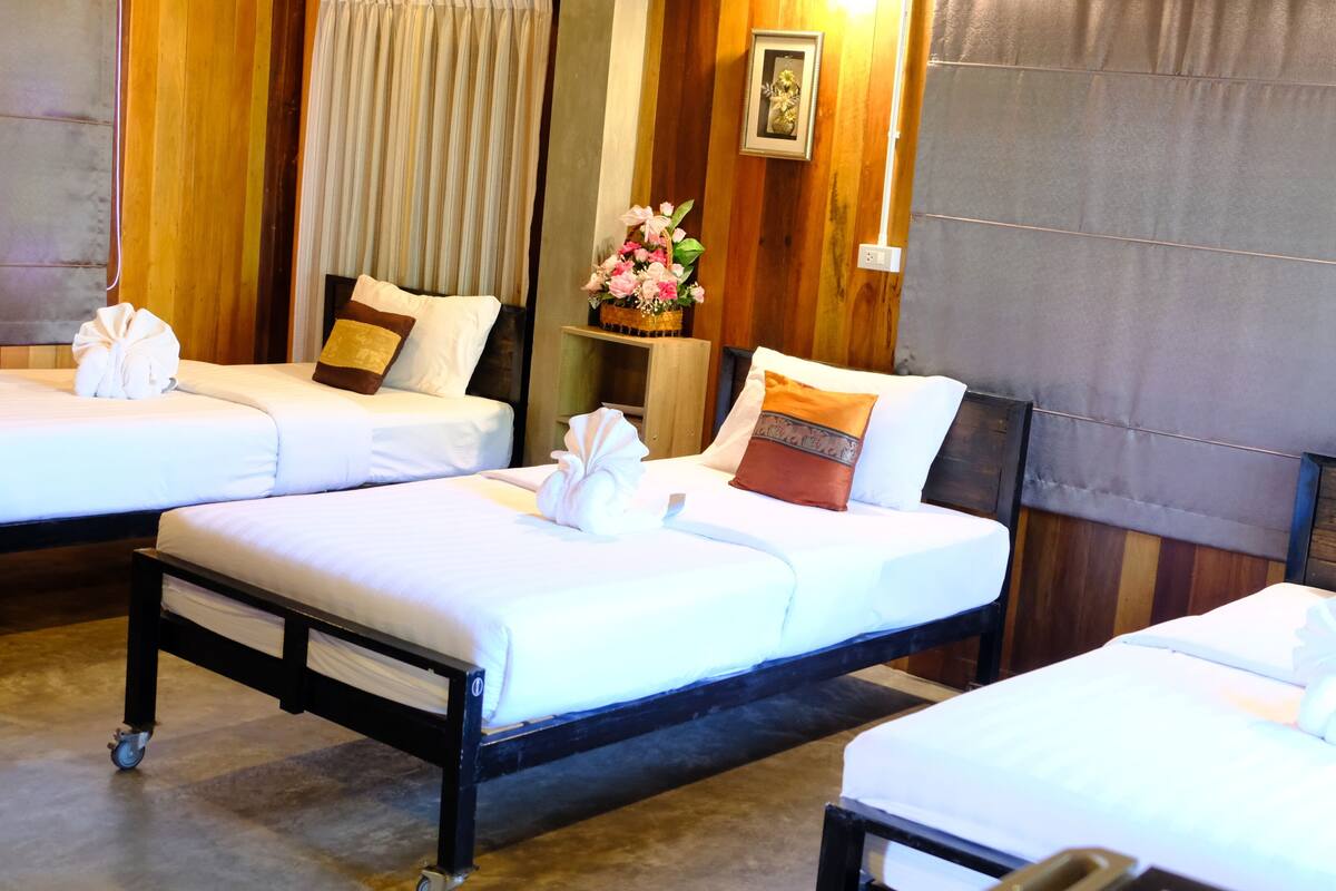 A hotel room with three beds, each with white linens and towels, wooden headboards, and a small table with a vase of flowers.