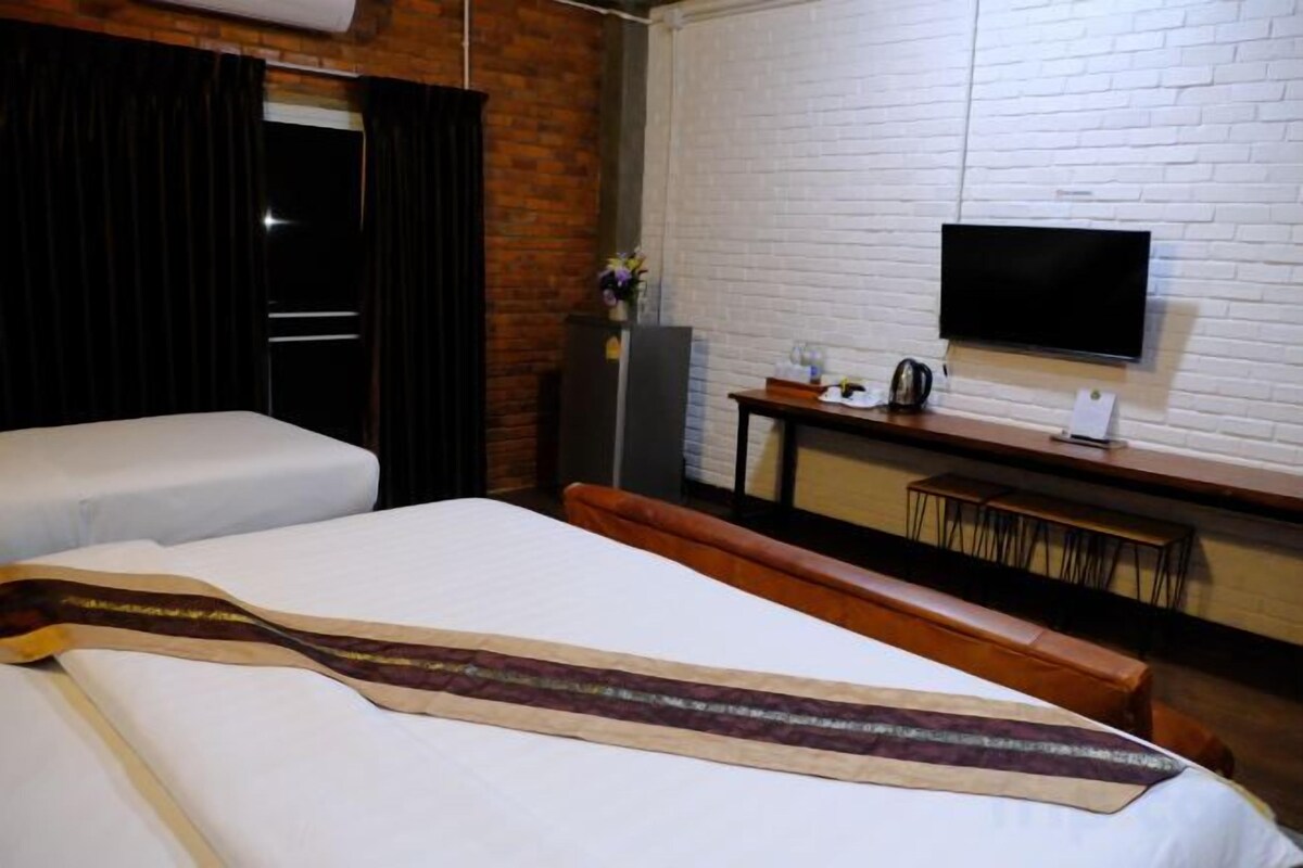 A hotel room with two beds, a flat-screen TV mounted on the wall, a desk with a chair, and a window with curtains.