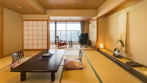 Una habitación japonesa tradicional con suelo de tatami, una mesa baja, un banco acolchado y una puerta corrediza que da a un balcón.