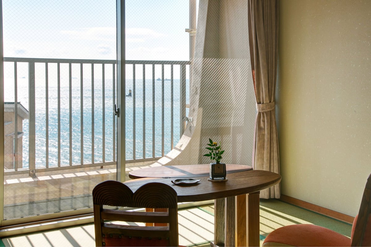 A balcony with a view of the sea, a table with a plant, and a chair.