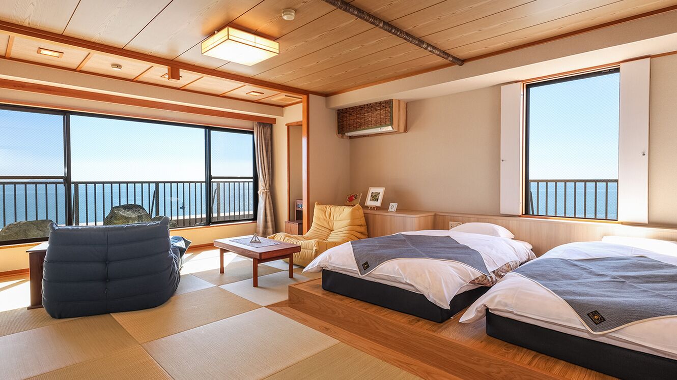 Ein Zimmer mit zwei Betten, einem Schlafsofa, einem kleinen Tisch und großen Fenstern mit Meerblick.