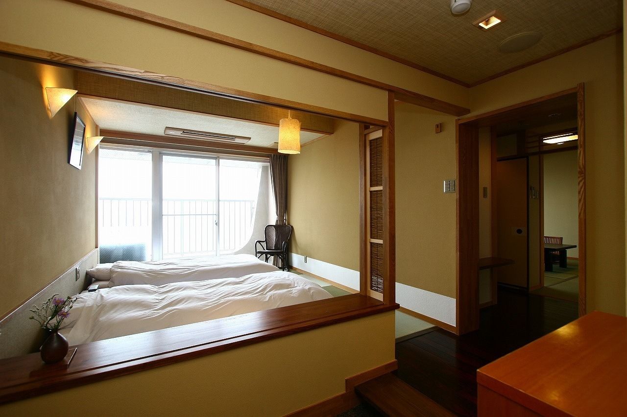 A hotel room with a bed, bedside table, and a window with curtains.